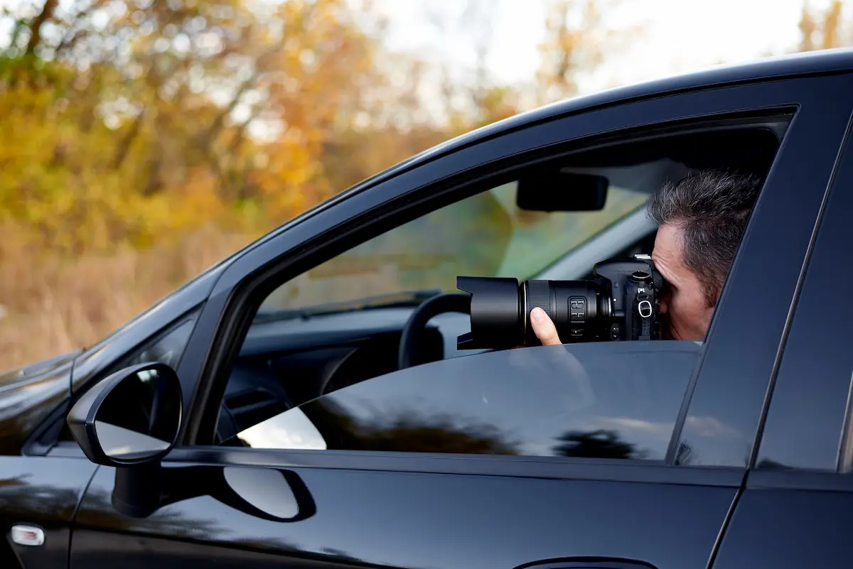 Hiring a private detective investigator conducting discreet surveillance from a vehicle using a professional camera in Singapore.